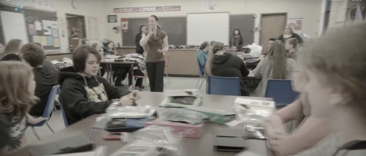 Classroom of children with adult woman standing in the middle.
